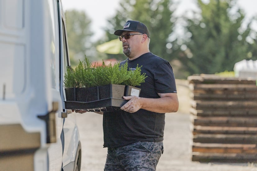 A crew member carrying a tray of young plants back to the van.