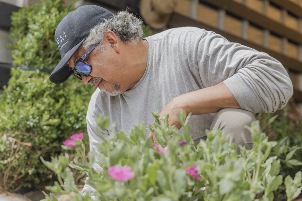 An R&M team member in a branded cap leaning in to inspect flowering perennials.