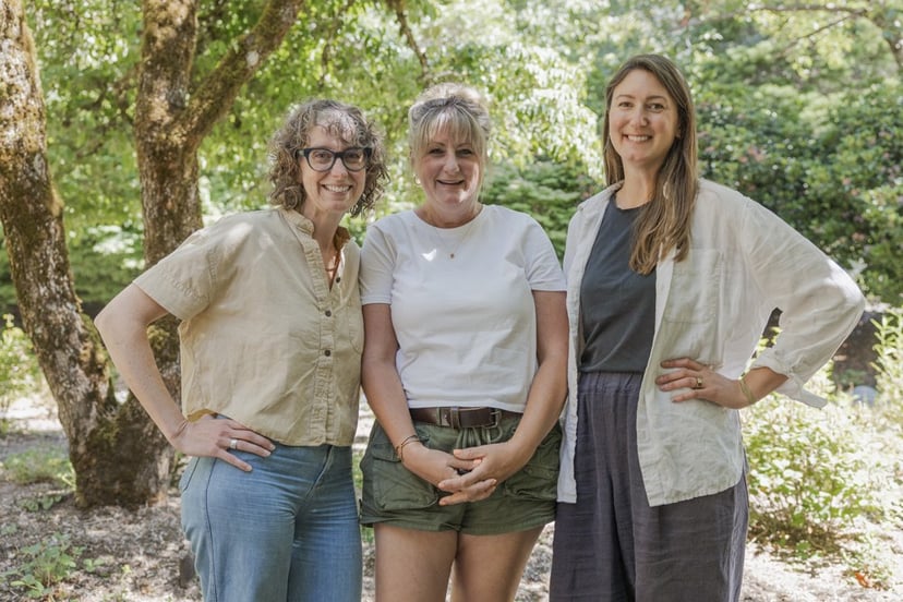 Three landscape designers standing together outdoors under a shade tree at a finished job site.